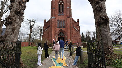 Jugendliche an der ersten Station des Kreuzwegs vor der Kirche St. Anschar in Münsterdorf. Auf einem gelben Tuch gelangen die Besucher in die Kirche.