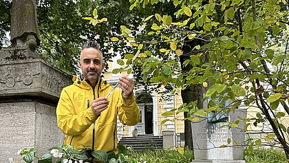 Propst Steffen Paar trägt seine gelbe Jacke und steht vor dem Neunerdenkmal in der Itzehoer Innenstadt. In der Hand hält er ein Band, das er in den Busch neben sich geknüpft hat.