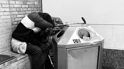 erschöpfter Mensch, traurig, müde und obdachlos neben einem Mülleimer zusammengekauert