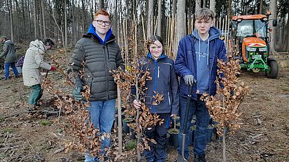 Drei Jugendliche stehen im Wald und nehmen an der Baumpflanzaktion teil