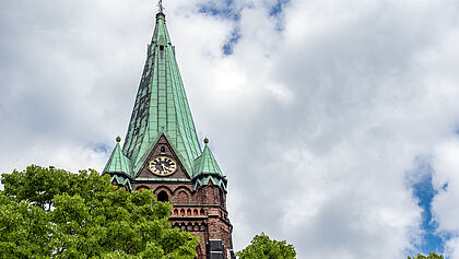 Kirchturm von St. Nikolai hinter einem Baum mit Wolken