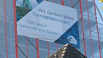 Ein Banner mit Dankesworten hängt an einem Gerüst des Kirchturms.