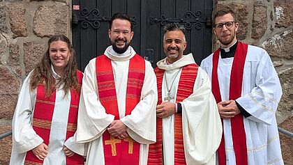 Pastorin Giulia Aman, Pastor Sven Voß, Propst Steffen Paar und Pastor Christoffer Klaas stehen in Alben vor dem Kirchenportal in St. Cyriacus Kellinghusen.