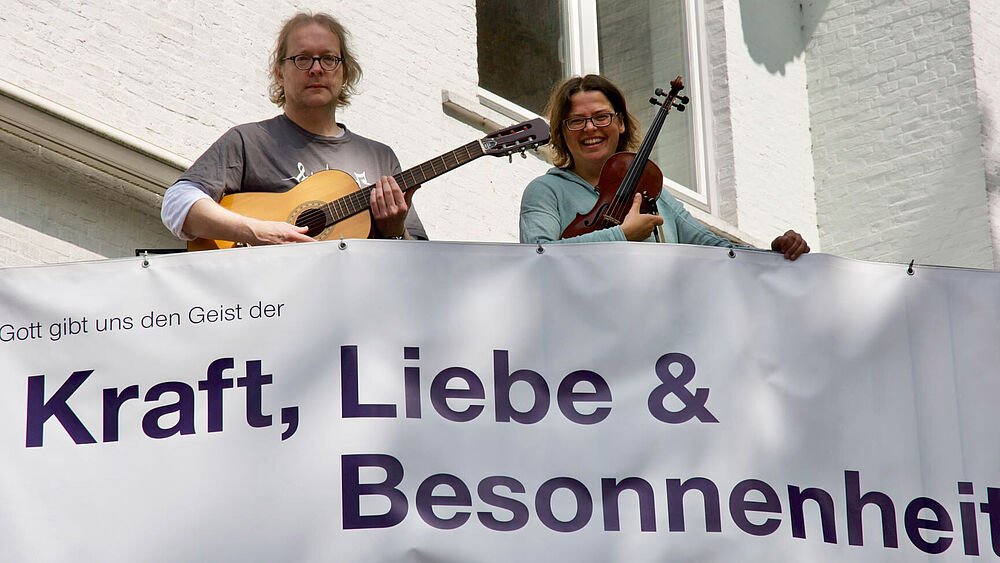 Die Regionalkantoren Dörte Landmesser und Stephan Reinke über dem Kirchenbanner mit der Aufschrift "Kraft, Liebe & Besonnenheit"