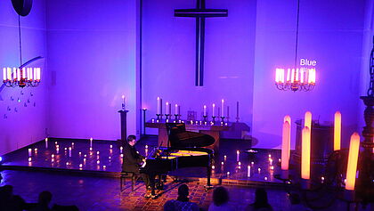 Ein Kirchenmusiker sitzt am Klavier inmitten von Kerzen. 