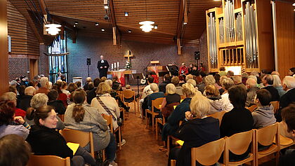 Blick in den Innenraum der Kirche, alle Plätze besetzt, vorn der Pastor im Talar. 