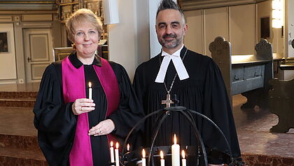 Pastorin Wiebke Bähnk und Propst Steffen Paar stehen in der St. Laurentii-Kirche in Itzehoe. Pastorin Bähnk hält eine Kerze in der Hand. Sie erinnern an das Ende des Zweiten Weltkrieges vor 80 Jahren.