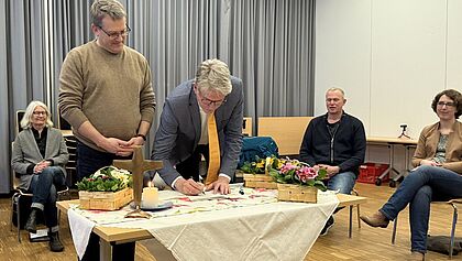 Zwei Gründungsmitglieder unterzeichnen an einem Tisch mit Tischkreuz