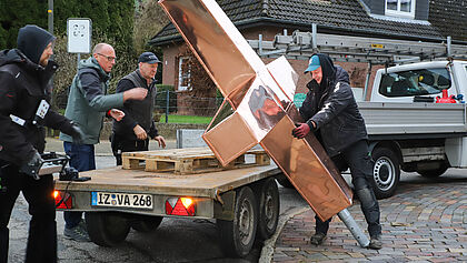 Kupferkreuz auf einem Anhänger, drumherum Bauarbeiter