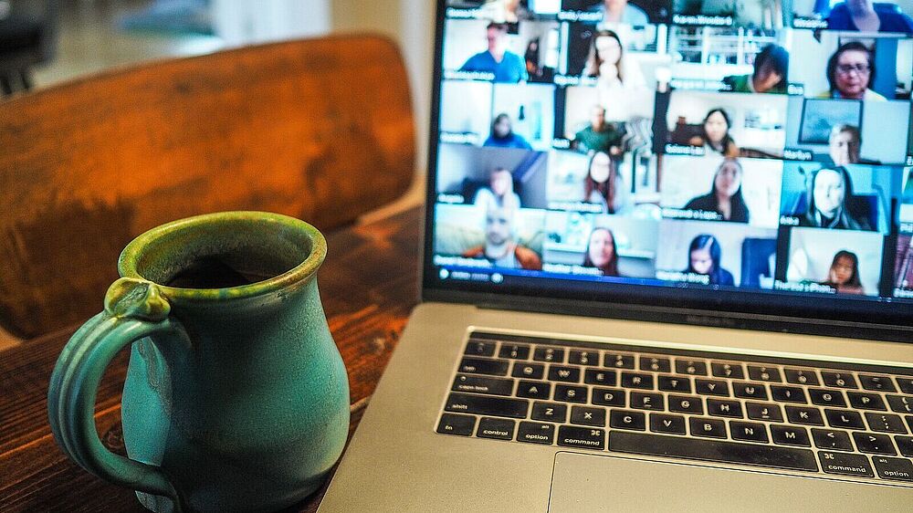 Aufgeklappter Laptop mit Videokonferenzkacheln auf dem Bildschirm und einer Tasse