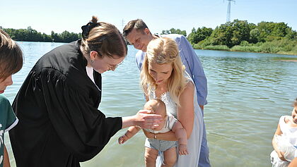 Pastorin tauft ein Baby in den Armen der Mutter am Fluss
