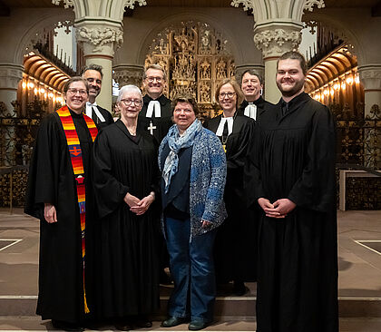 Gruppenfoto in einer historischen Kirche: Mehrere Personen in liturgischen Gewändern stehen vor einem reich verzierten Altar. Die Szene wirkt feierlich und offiziell, typisch für kirchliche Veranstaltungen wie Gottesdienste, Ordinationen oder besondere Gemeindefeiern. Die Architektur mit Säulen, Altarschmuck und warmem Licht verstärkt die sakrale Atmosphäre.