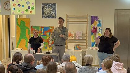 In der großen Bewegungshalle der Kita-Mose fand die Kunst-Aktion der Kita statt. Moderator Gerrit Hoss schwang den Hammer. Hier bieten die Anwesenden auf ein Kunstwerk, das eine Erzieherin präsentiert.