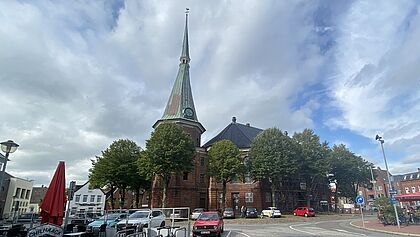 Die St. Bartholomäuskirche im Stadtkern von Wilster umringt von Bäumen im Sommer.