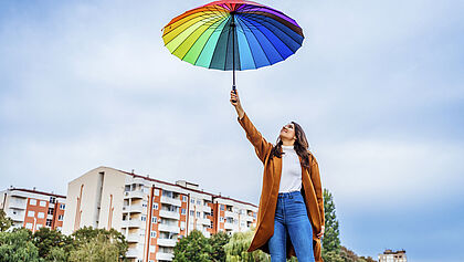 Frau mit buntem Regenschirm in einem Wohngebiet