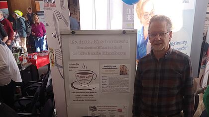 Pastor an einem Stand, der mit dem Namen Altersseelsorge gekennzeichnet ist