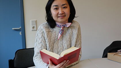 Kirchenmusikerin Xiaojing Sheng sitzt mit dem Evangelischen Gesangbuch vor einem Tisch 