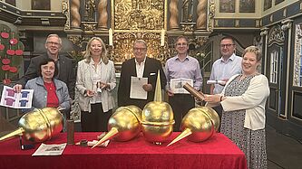 Sieben Personen stehen hinter dem Altar, auf dem sich auf einer roten Tischdecke goldene Turmkugeln befinden