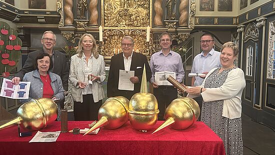 Sieben Personen stehen hinter dem Altar, auf dem sich auf einer roten Tischdecke goldene Turmkugeln befinden