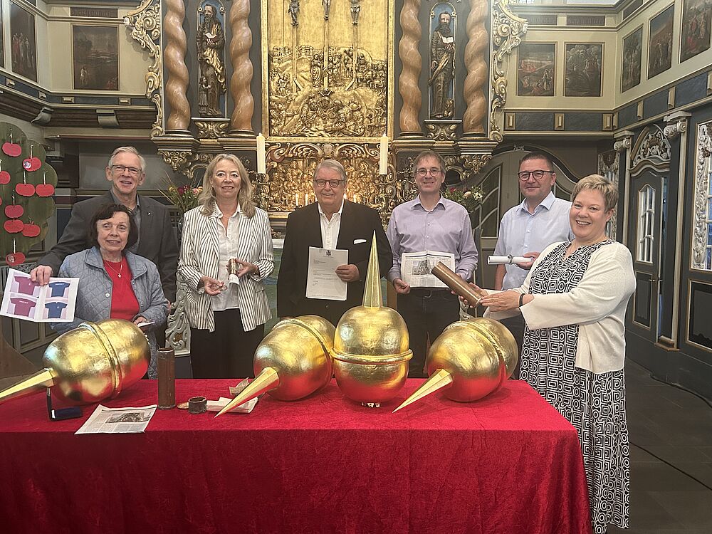 Sieben Personen stehen hinter dem Altar, auf dem sich auf einer roten Tischdecke goldene Turmkugeln befinden