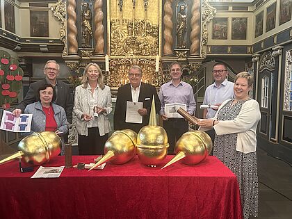 Sieben Personen stehen hinter dem Altar, auf dem sich auf einer roten Tischdecke goldene Turmkugeln befinden