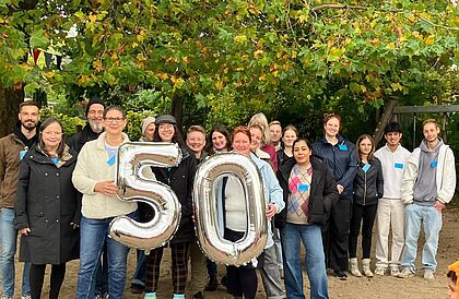 Das Team der Evangelisch-Lutherischen Kita Fehrsstraße posiert lachend mit einer aufblasbaren 50.