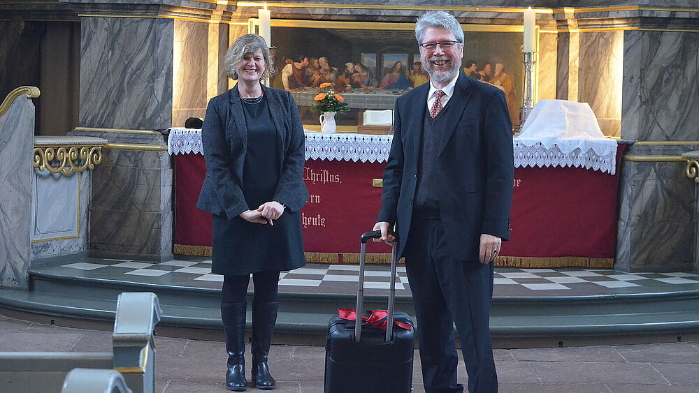 Pastor Wolfgang Schulz mit Koffer vor dem Altar in der Kirche zu Wilster