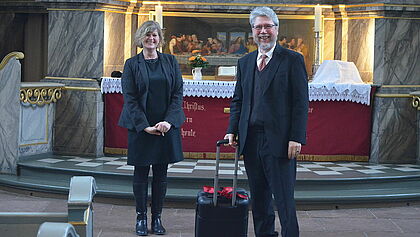 Pastor Wolfgang Schulz mit Koffer vor dem Altar in der Kirche zu Wilster