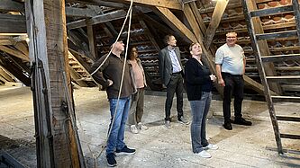 5 Personen stehen im Gebälk eines Glockenturms.