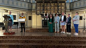 Eine Gruppe Menschen steht im Altarraum der Itzehoer St. Laurentii-Kirche. Gleich werden Dankesblumensträuße verteilt.