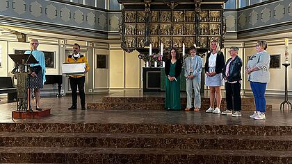 Eine Gruppe Menschen steht im Altarraum der Itzehoer St. Laurentii-Kirche. Gleich werden Dankesblumensträuße verteilt.