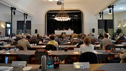 Synodentagung im Coloseum, Wilster: Synodale sitzen an Tischen, auf der Bühne sitzt das Präsidium