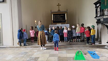 Kinder stehen mit Erzieherin vor dem Altar in einer Kirche. 