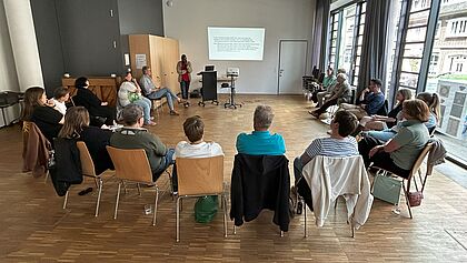 Eine Gruppe von 18 Personen sitzt im Kreis um Dr. James Karanja, der einen Vortrag über Rassismus in der Partnerschaftsarbeit hält.