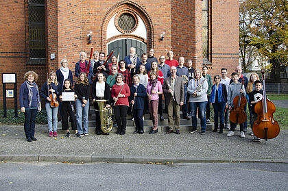 Musikerinnen und Musiker stehen vor der Thomaskirche in Elmshorn und schauen fröhlich in die Kamera