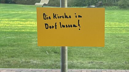 Zettel klebt am Fenster mit der Aufschrift "Die Kirche im Dorf lassen"