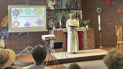 Pastorin mit Albe und buntem Blumenschmuck im Schlager-Stil