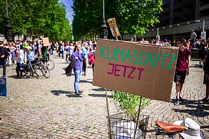 Blick auf eine Demonstration, wo ein Plakat mit der Aufschrift Klimaschutz jetzt zu sehen ist