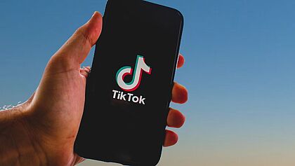 Es wird ein Handy mit dem TikTok-Logo wird in die Luft gehalten
