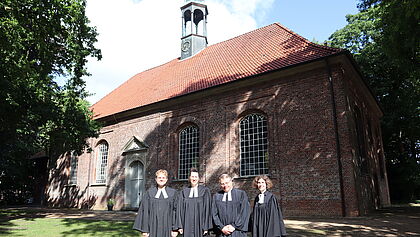 Vier Pastor:innen im Talar vor der Kirche St. Jürgen in Horst