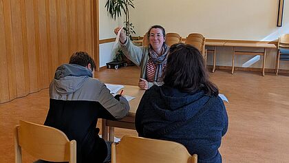 Pastorin Miriam Pietzsch sitzt bei der Anmeldung im Gemeindesaal mit einem Jungen und seiner Mutter am Tisch.